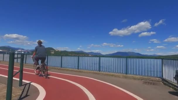 Pemandangan Kembali Wanita Mengendarai Sepeda Sepanjang Danau Arona Dan Pelabuhan — Stok Video