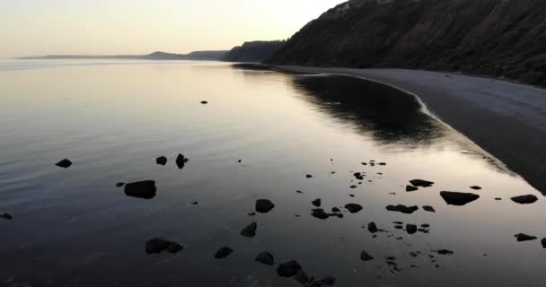 空中平静平静宁静夕阳西下的水面旁边是小卵石射击海滩 慢速向前冲 — 图库视频影像