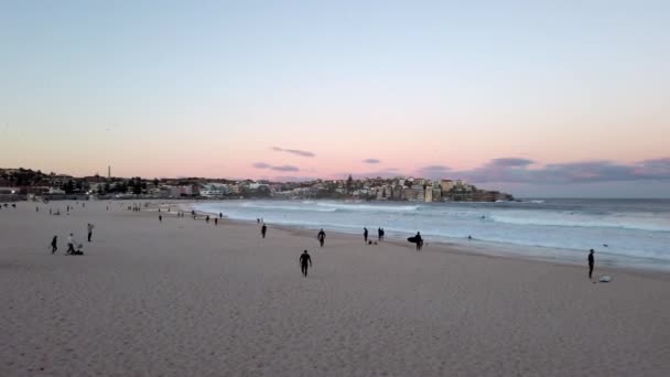 ニューサウスウェールズ州シドニーの日没時の背景に都市景観を持つボンディビーチの砂浜の人々オーストラリア ワイドショット — ストック動画