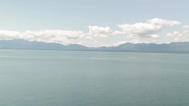 ブリティッシュ コロンビア州のホーンビー島の海のすぐ向こうの背景にあるロッキー山脈を眺めるヘリウェル草原の崖の端に立つカナダ — ストック動画