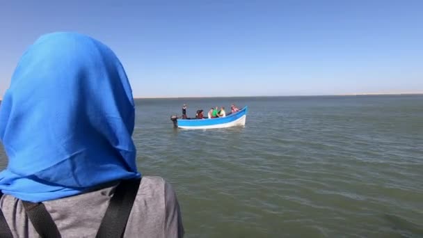 女性がモロッコのタルファヤ県で女性が見ている間 ナイララグーンの港を離れる漁船の映画撮影 — ストック動画