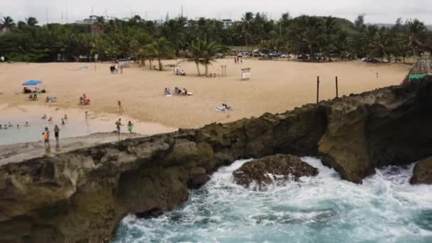 プエルトリコのアレシボにあるLa Poza Del Obispo Beachで泳ぐ人々とロッキー海岸で波がクラッシュします 空中後退 — ストック動画