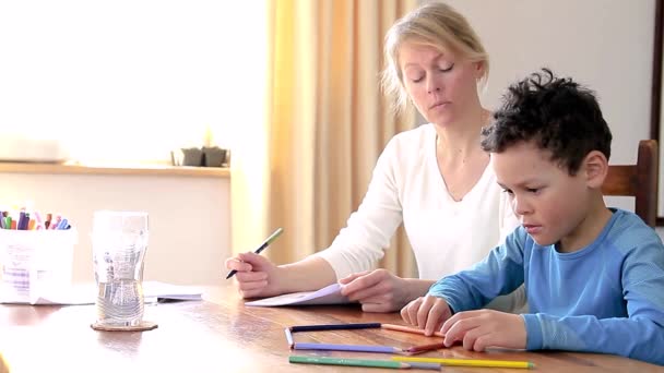 fiú csinál házi feladat tanulás otthon anya a gyermek ül egy asztalnál stock videó