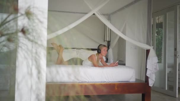Frau entspannt sich auf Hotelbett und hört Musik mit Handy
