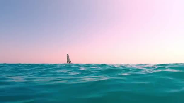 背景为粉红蓝绿色大海中航行的小帆船的低角度海平面视图 — 图库视频影像