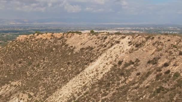 緑のスペインの田舎の農場のフィールドを明らかにするために乾燥砂漠の丘の中腹を飛ぶドローン — ストック動画