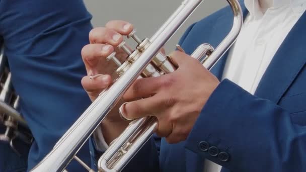 Close-up of hands, of musician in blue suit, playing silver trumpet