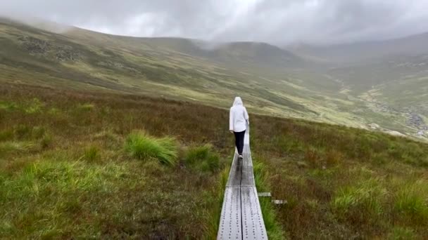 在朦胧的云雾天气和灰蒙蒙的天气里 在爱尔兰绿色山景之间的木制狭窄小径上漫步的慢镜头 — 图库视频影像
