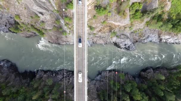 阳光明媚的日子 不列颠哥伦比亚省北部的Hagwilget峡谷桥垂直向下俯瞰 当汽车驶过桥下时 慢慢上升无人驾驶飞机的镜头 冰川河水流得很快 — 图库视频影像