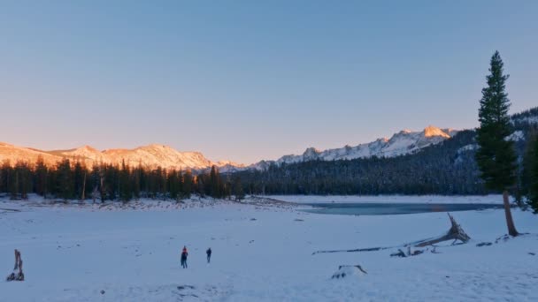 遠くの人々と雪のマンモスの馬蹄形の湖小さな丘と太陽の光の山と澄んだ夕日の空の背景を歩く — ストック動画