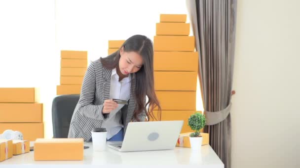 Asijská žena obdržela velkou platbu na kartě zůstatek dělá on-line prodej se svým notebookem, kurýrní balíčky na domácí kanceláři