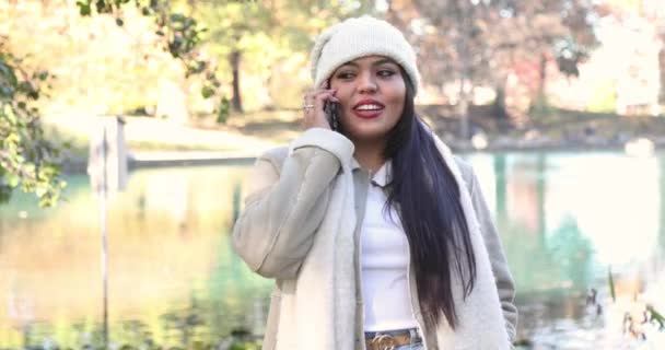 在寒冷的秋秋季节 女人在城市公园打电话时得到了好消息 大学生 被大学录取了 她穿着一件白色的夹克和贝尼 在4K内开枪 — 图库视频影像