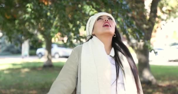 美丽的姑娘看着周围寒冷的秋天落叶 惊讶地微笑着看着一个城市公园 她穿着一件白色的夹克 头戴便帽 以4K慢动作射击 — 图库视频影像