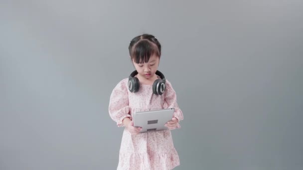 带着耳机的亚洲小女孩喜欢在网上看平板电脑上的视频 高兴地跳舞 — 图库视频影像