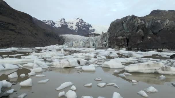 氷河とアイスランドの雪に覆われた山脈から砕けた浮遊する氷山のドローンの眺め — ストック動画