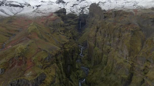 从空中俯瞰冰岛北冰洋的深谷 无人机飞越峡谷和峡谷内狭窄的溪流 背景是雪山 — 图库视频影像