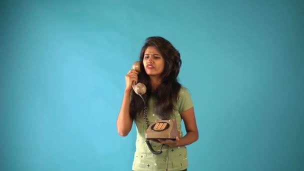 オレンジ色の岩の中に立っている若いインド人の女の子は 古いヴィンテージの電話で怒って隔離された青の背景で話しています 人々の感情ライフスタイルのコンセプト — ストック動画