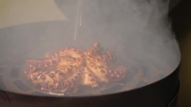 Cinematic slow motion shot of chef using tongs to transfer a perfectly cooked, mouthwatering golden brown octopus from a barbecue smoker to a chopping board with piping hot aromatic smokes rising up.