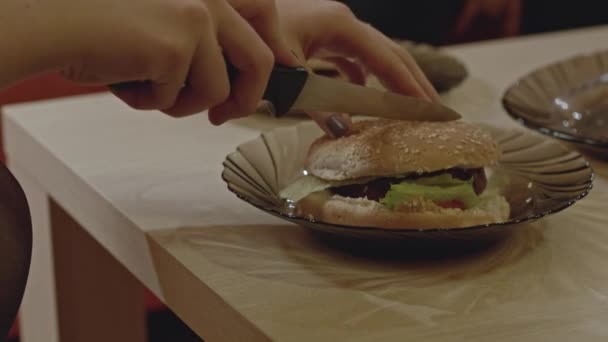 Vrouwen Handen Snijden Een Hamburger Tweeën Met Een Mes Tafel — Stockvideo