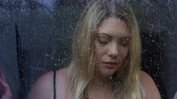 沮丧的金发女人透过窗户望着雨中的树木 — 图库视频影像