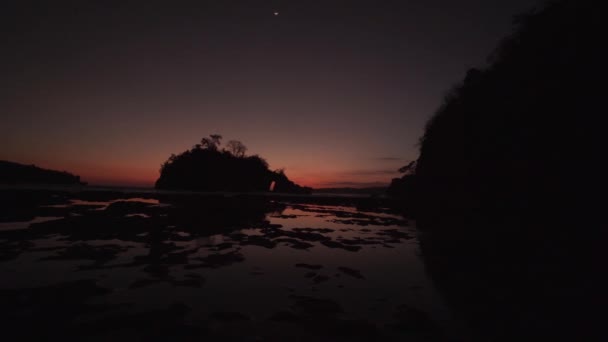 インドネシアのヌサペニダ島の海にある大きな岩の後ろの太陽の最後のビットの遅いパン4K — ストック動画