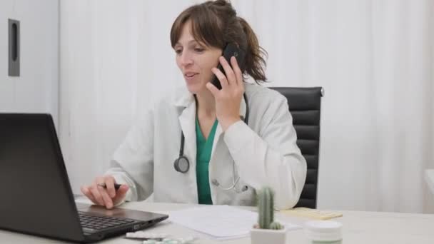 Žena lékař mluvit s telefonem při prohlížení na svém notebooku v její klinice. široký záběr