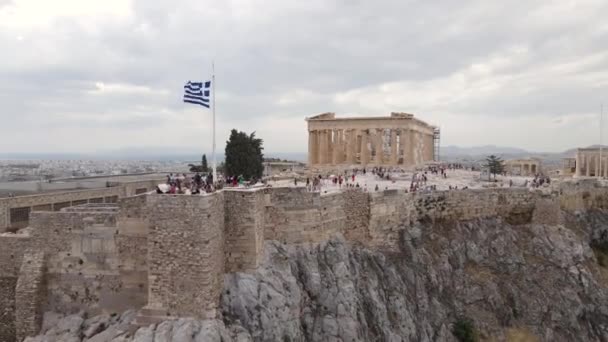 ギリシャのアテネ 古代アクロポリスの空中ビュー ギリシャの旗や有名なランドマークを訪問人々 バックドローンショットを引く — ストック動画