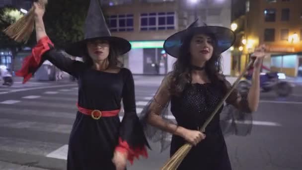 两个身穿女巫万圣节礼服的哥伦比亚女孩 晚上站在城市人行道上看着相机微笑 中型闭路射击 — 图库视频影像