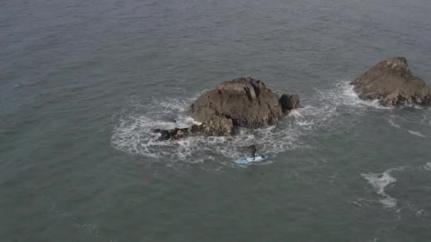 Sup运动员在岩石海洋小岛附近的混沌水中划桨的空中 — 图库视频影像