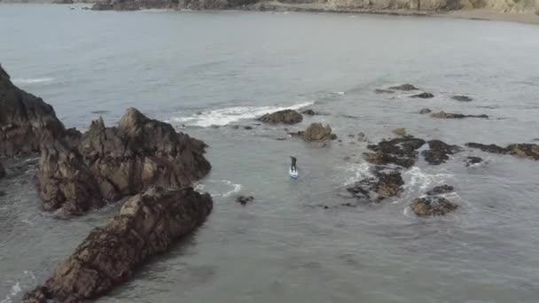 空中降落到海洋中锯齿状岩石中的雄性桨板上 — 图库视频影像
