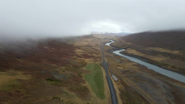 左から川の流れと高速道路の右側からの空中の景色車は山脈に覆われた雲でアイスランドの北極の風景を通過しています — ストック動画
