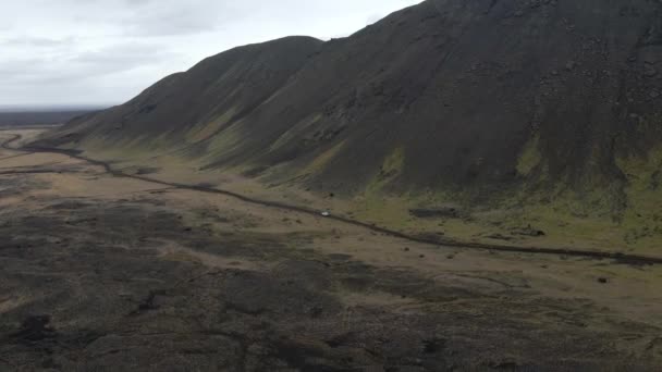 在冰岛 无人驾驶飞机正沿着一辆白色的汽车在由黑色沙滩和高山构成的崎岖的路上巡游时跟踪着一辆白色的汽车 空中射击 — 图库视频影像