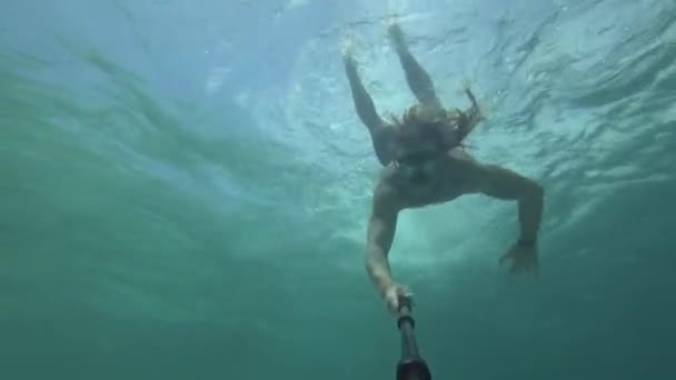 一个年轻 留着长发 留着长胡子的男人 带着浮潜的护目镜 从水面跳下去 跳入生机勃勃的水里 穿过礁石之间狭窄的空间 — 图库视频影像