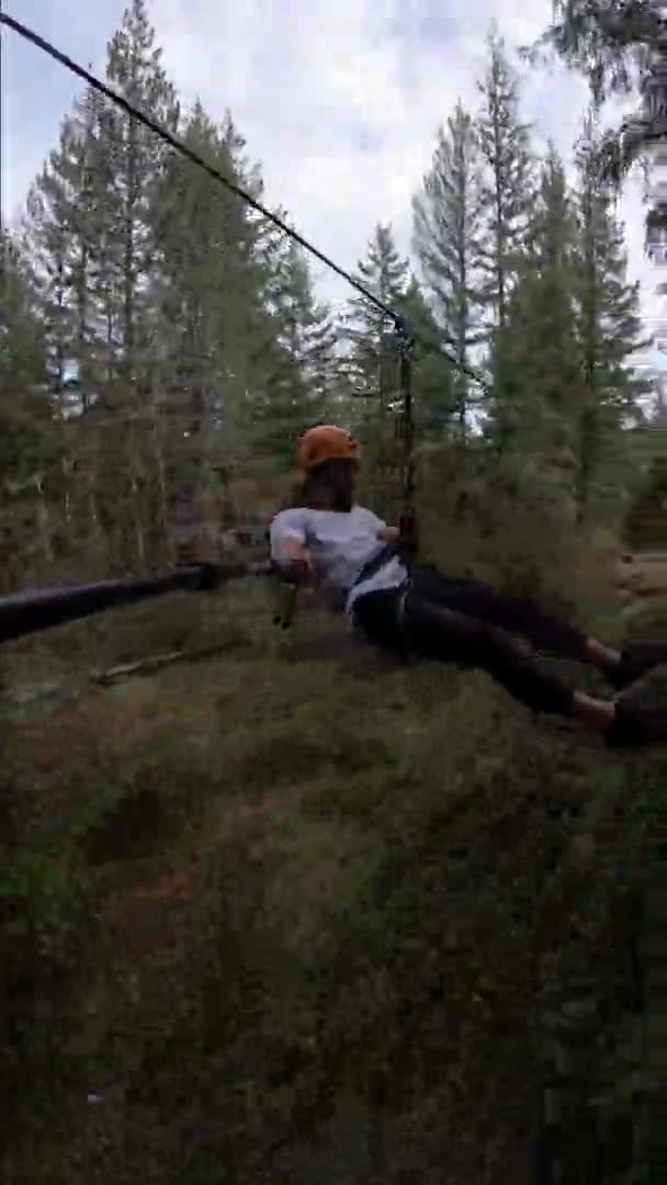 カナダのジップラインで高速滑降する若い男の垂直アクションカメラショット彼の周りの美しい緑豊かな森 彼は笑ってる — ストック動画