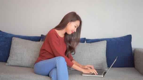 Asiática Sonriente Mujer Joven Sentada Sofá Utilizando Portátil Portátil Mirando — Vídeos de Stock