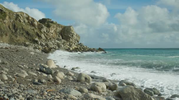 4K在阳光灿烂的日子里 在英国波特兰多塞特的Church Ope海滩上拍到海浪拍到岩石的慢镜头 背景是悬崖峭壁 — 图库视频影像