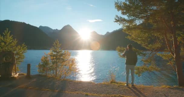 男性の観光客は オーストリア ヨーロッパで日没の黄金の時間で湖Achenseeでアルプスの山々の景色を記録します — ストック動画