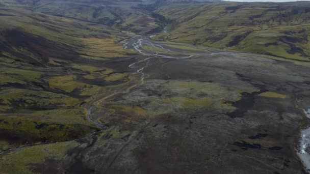 谷に流れる狭いストリームの空中ビュー アイスランドの北極の風景の上を 曇り空で飛行するドローン 背景に雪の山のキャップ — ストック動画