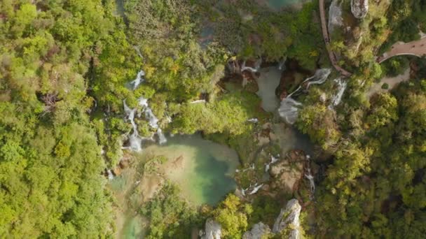 岩の多い崖と鬱蒼とした森の間の滝に接続された明るいターコイズブルーの湖の信じられないほどの空中ドローントップダウンビュー カメラはズームアウトし 立ち上がり 後方へ移動します 4K映像 — ストック動画
