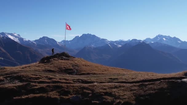 Männlicher Alleinwanderer Besteigt Berggipfel Mit Schwenkender Schweizer Flagge Und Epischer — Stockvideo