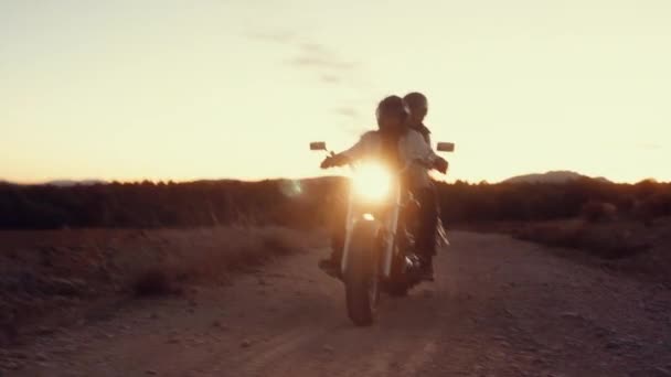 夕暮れ時にヘッドライトからまばゆい光で田舎道でバイクに乗るカップル — ストック動画