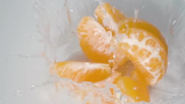 Close Geschilde Mandarijn Sinaasappel Valt Water Splitst Plakjes Witte Achtergrond — Stockvideo
