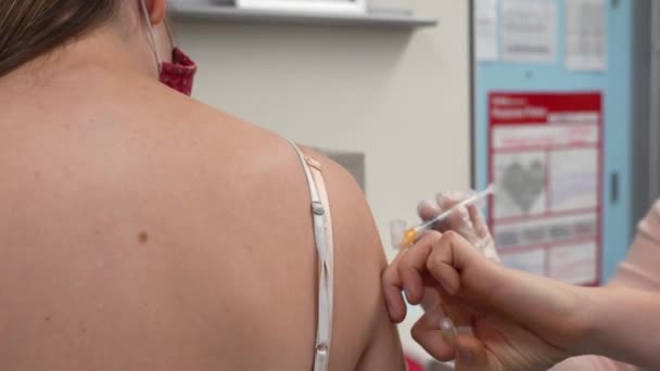 COVID 19 Vaccine Booster Shot in the Arm of Young Adult Female Woman Wearing a Medical Mask, Corona Virus Injection Administered by Nurse in Shoulder in Pharmacy with No Face of the Patient or Person