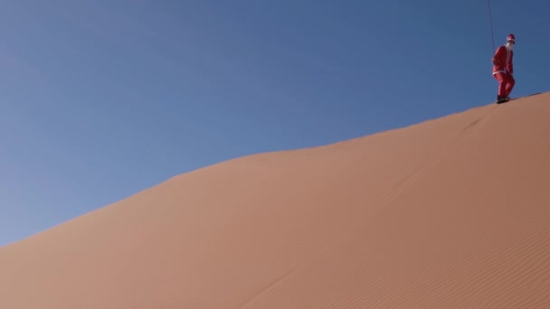 Sandboarding on the dunes of the Sahara Desert in Africa Dressed as Santa - Static Wide Shot