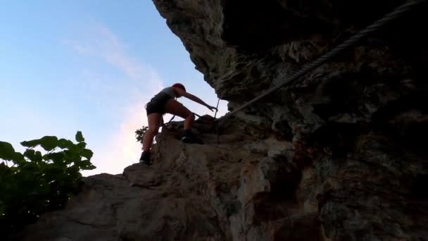一个穿着黑色热裤和长腿的女孩爬上岩石 你可以看到她在蓝天下的轮廓 — 图库视频影像