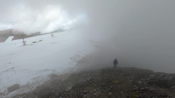 大きな灰色の雲に岩を歩いている登山家の非常に映画的な映像 山の左側は雪に覆われている — ストック動画