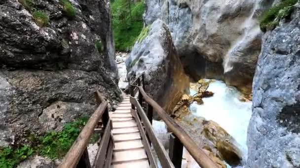 美しい渓谷の野生の白い川の横にある2つの岩の間に木製の階段を歩いて誰かの滑らかなPov映像 — ストック動画