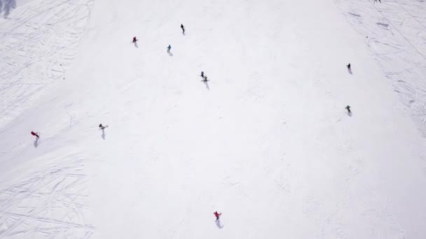 4K空中映像スキー場のスキー場のスキーヤーに続くドローン 高い山の中で冬の日の間にスキー場を滑降 空中ビューアルプス — ストック動画