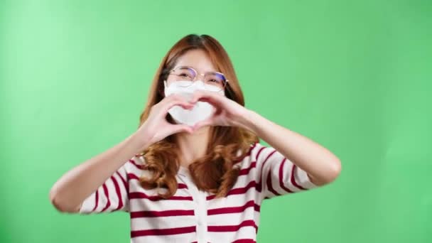 Young man with eyeglasses making heart symbol with hands in studio with chromakey.