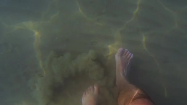砂の雲を上げる太陽の反射と砂の海底に水中を歩く人の足や足のFpvビュー スローモーション — ストック動画